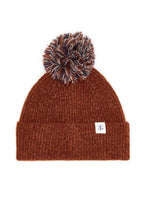 A brown ribbed knit beanie hat with a matching brown, black, and white pom-pom on top, featuring a small white brand tag on the side cuff.