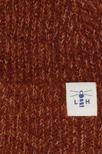 Close-up of a brown ribbed knit fabric with a small white sewn label featuring a blue lighthouse logo and the letters 'L H'.