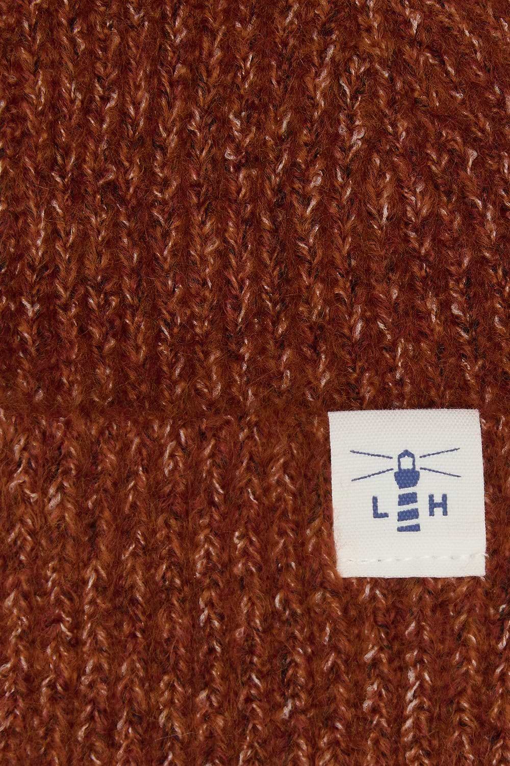 Close-up of a brown ribbed knit fabric with a small white sewn label featuring a blue lighthouse logo and the letters 'L H'.