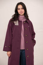 Woman wearing a long purple coat over a pink sweater with a white background