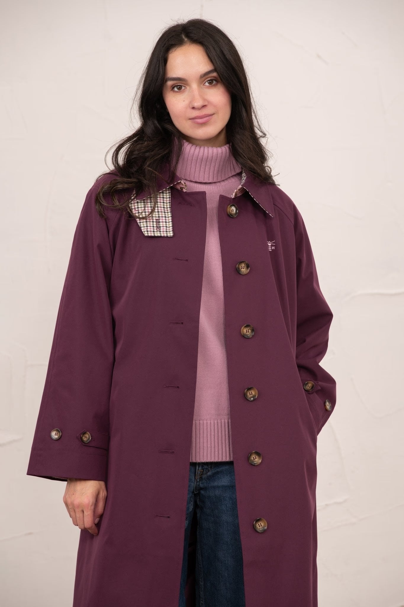 Woman wearing a long purple coat over a pink sweater with a white background