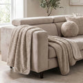 A light beige sofa in a bright living room, styled with a chunky cEllis Throw in Minkdraped over the arm and seat, and a matching round throw pillow.
