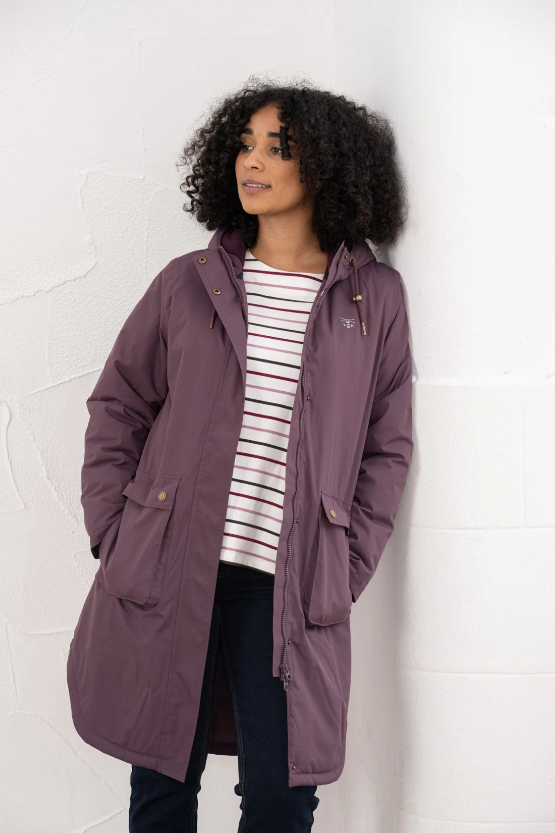 Woman wearing a long purple coat against a white wall