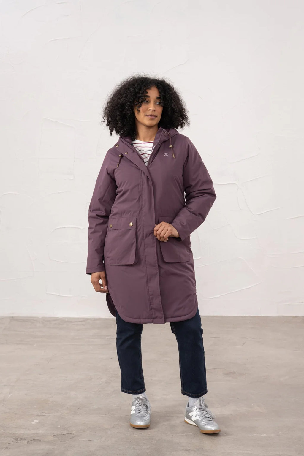 Person wearing a purple coat standing against a white wall.