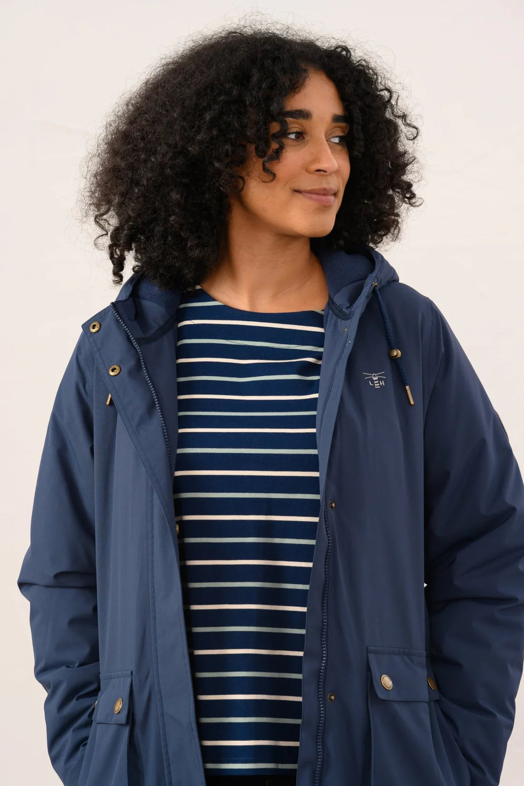 Woman wearing a navy blue hooded jacket over a striped shirt on a white background