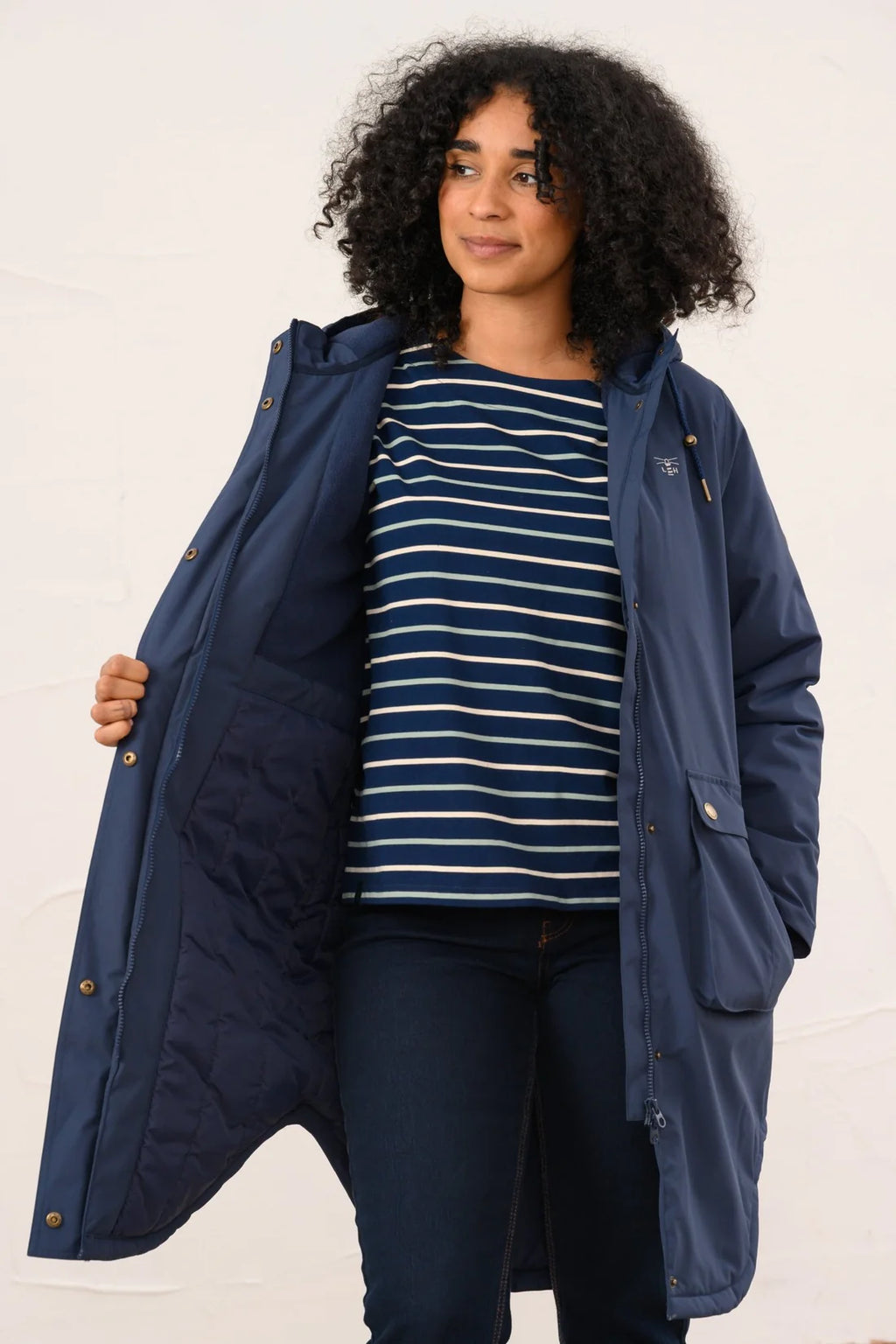 Woman wearing a navy blue coat over a striped shirt on a white background