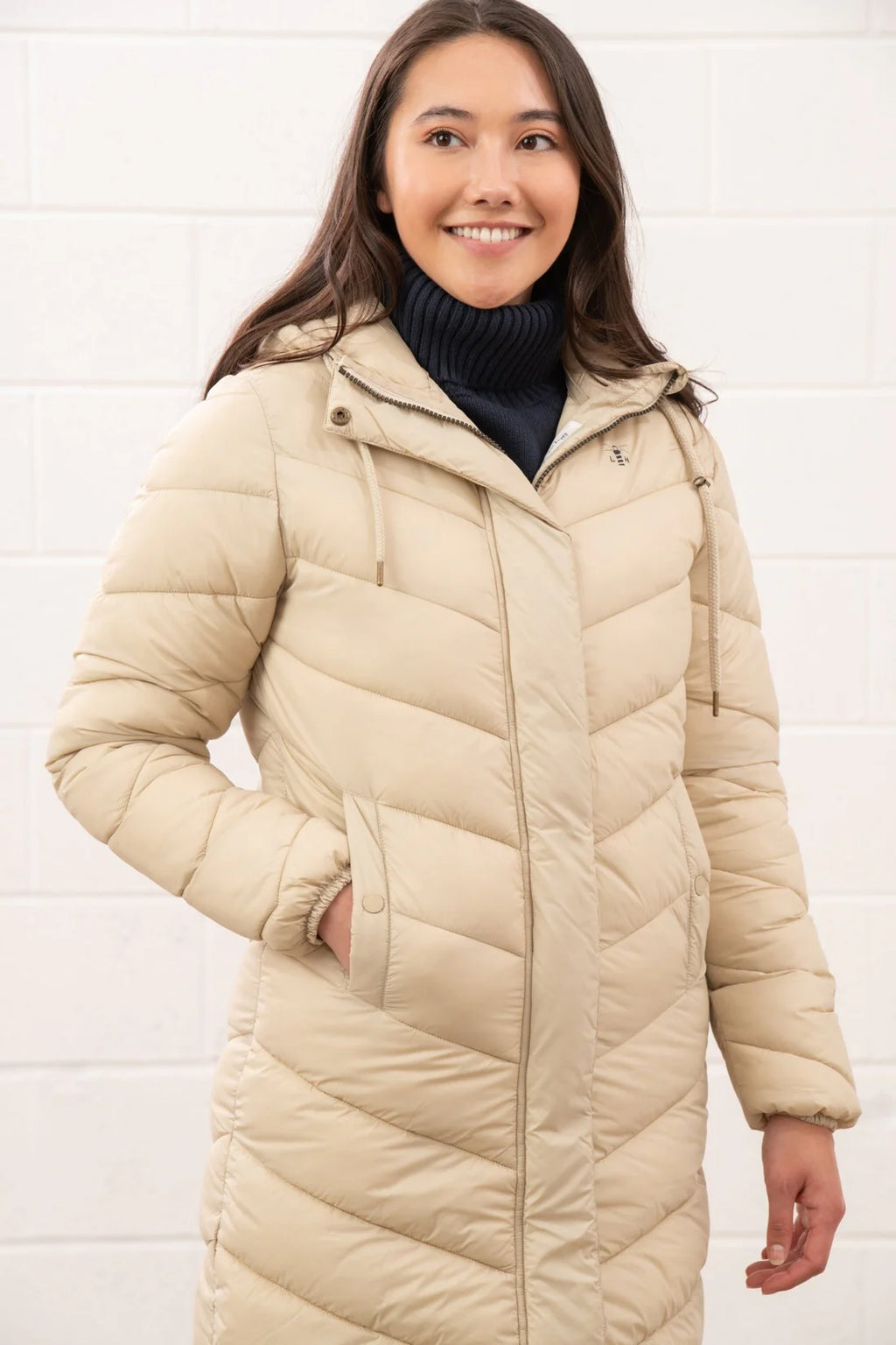 Woman wearing a beige puffer coat over a dark turtleneck against a white background