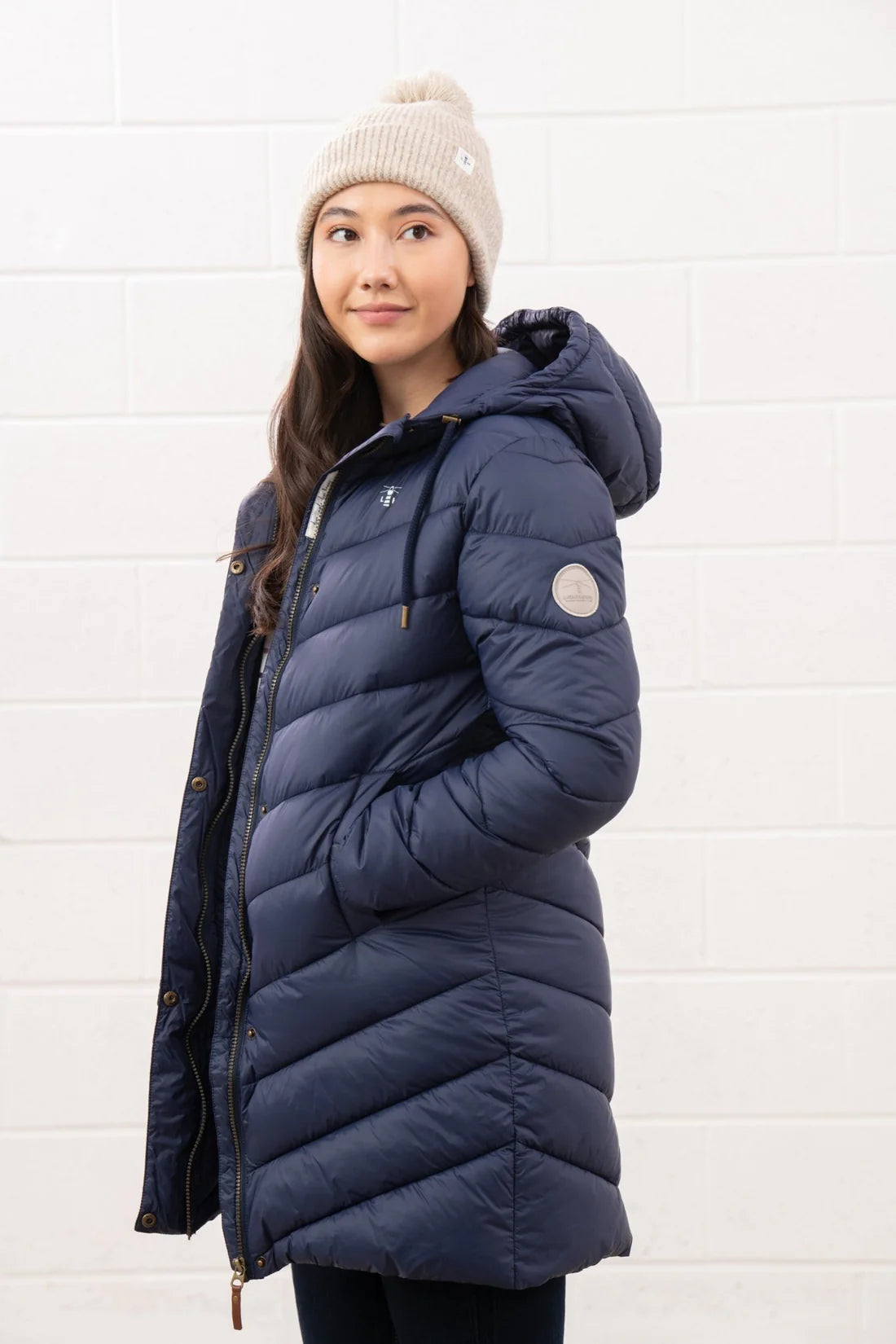 Woman wearing a blue puffer coat and beige beanie against a white background