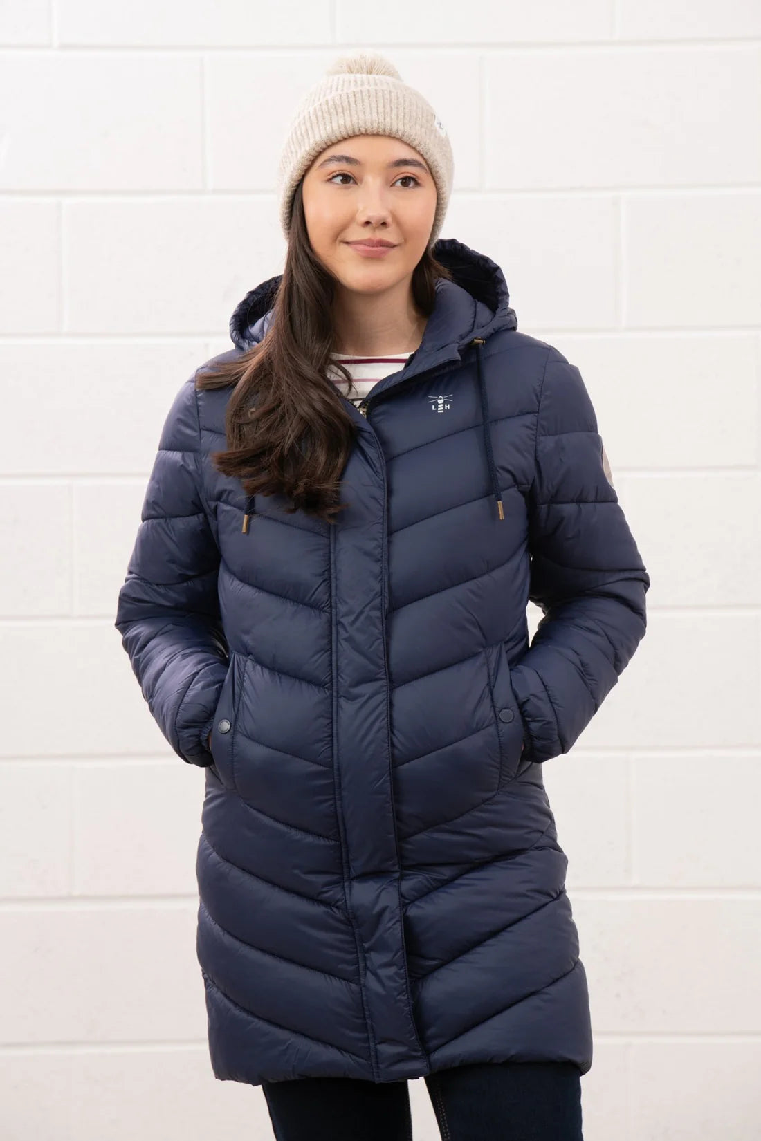 Woman wearing a blue puffer coat and white beanie against a white wall
