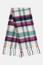 A soft woven scarf with a plaid pattern in white, dusty pink, teal green, and navy blue, finished with fringed ends, shown against a plain light gray background.