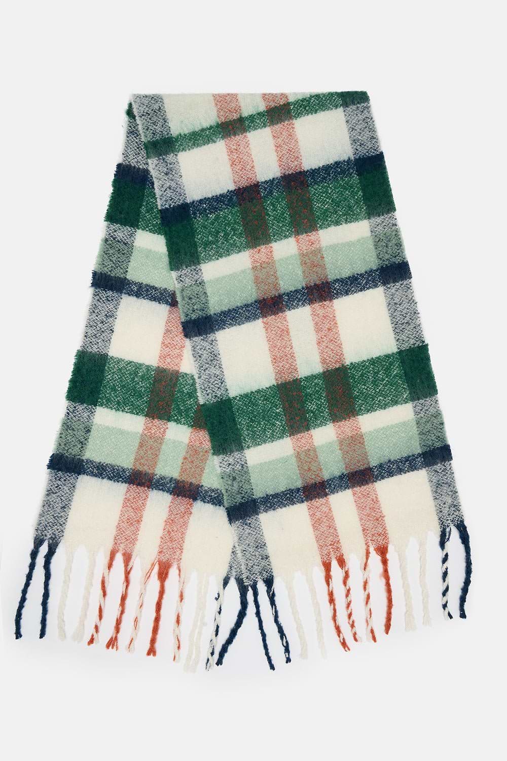 A folded plaid scarf with fringed ends, featuring a pattern of green, navy, dusty red, and cream stripes on a light background, set against a plain light gray backdrop.