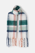 A soft, fuzzy plaid scarf with fringe ends, featuring a pattern of white, dark green, light blue, and muted orange on a clean white background.