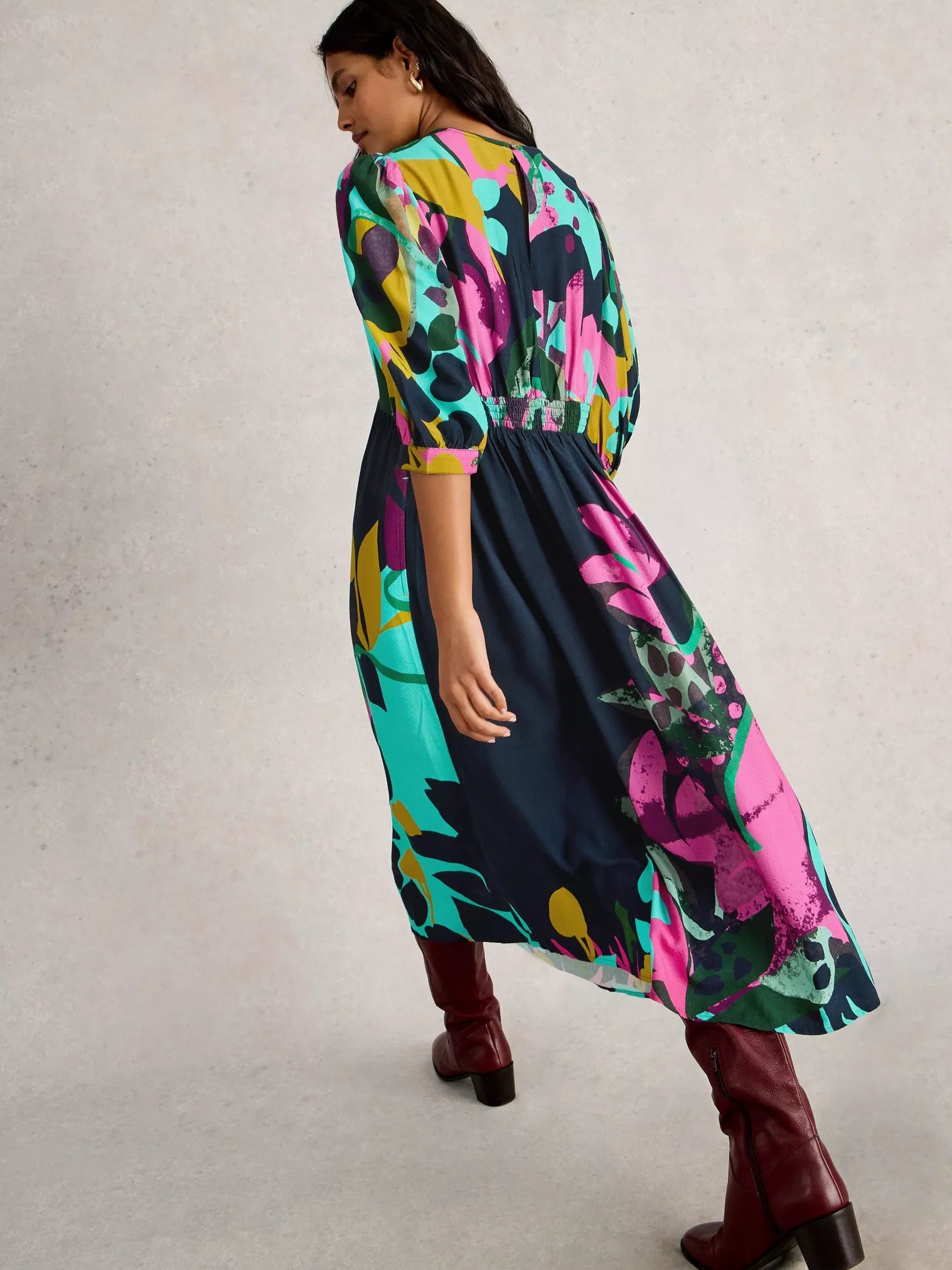 Woman wearing a colorful floral dress with maroon boots on a plain background