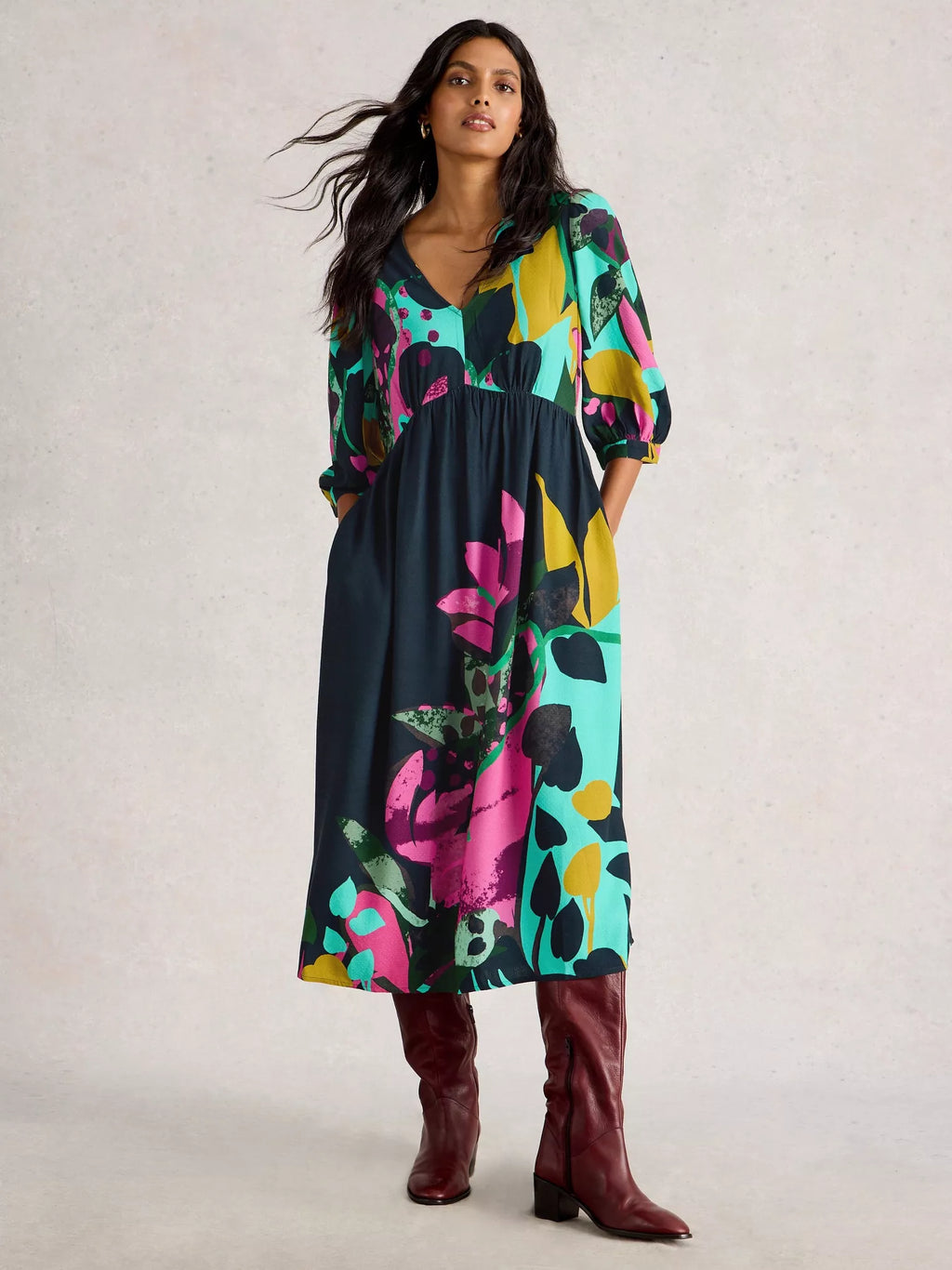 Woman wearing a colorful floral dress with brown boots on a light background