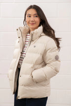 Woman wearing a beige puffer jacket against a white wall