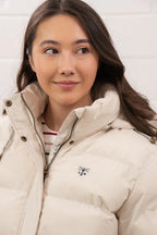 Woman wearing a beige puffer jacket with a visible brand logo on a white background