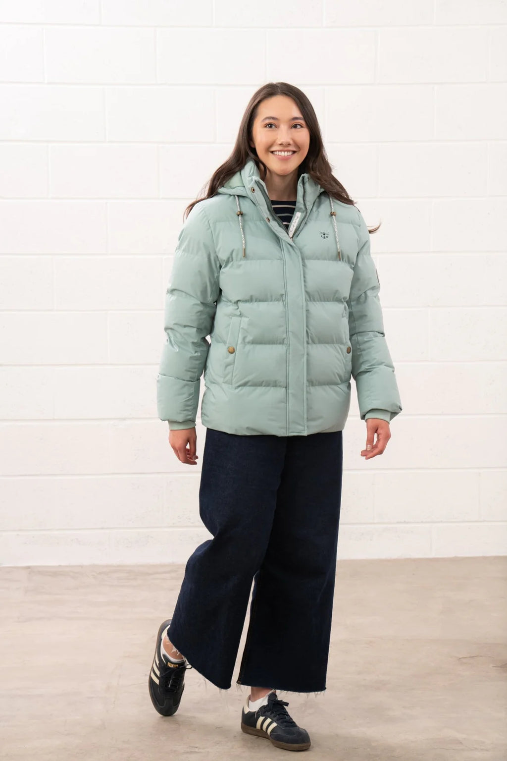 Woman wearing a light green puffer jacket against a white background