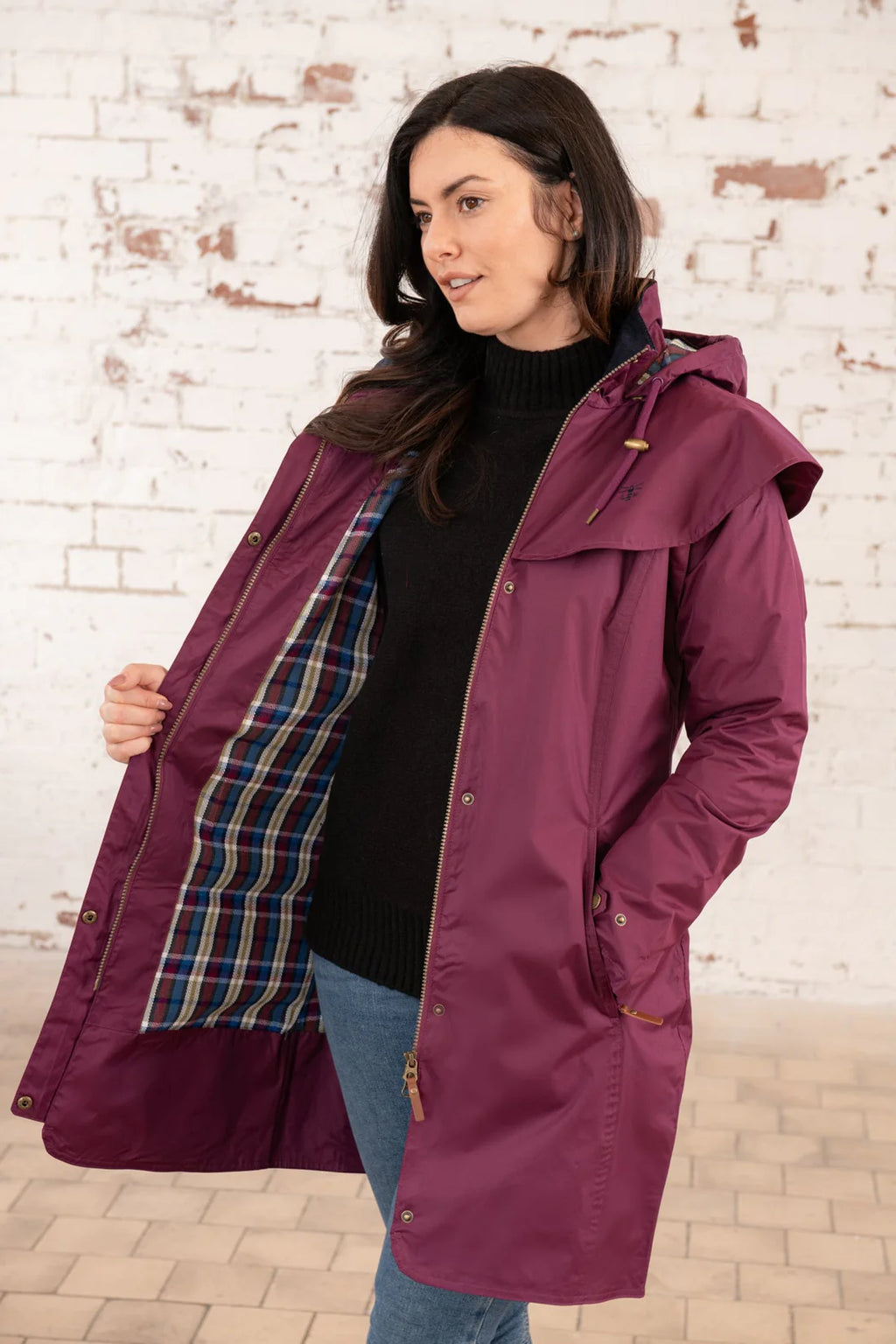 Woman wearing a purple raincoat with plaid lining against a brick wall.