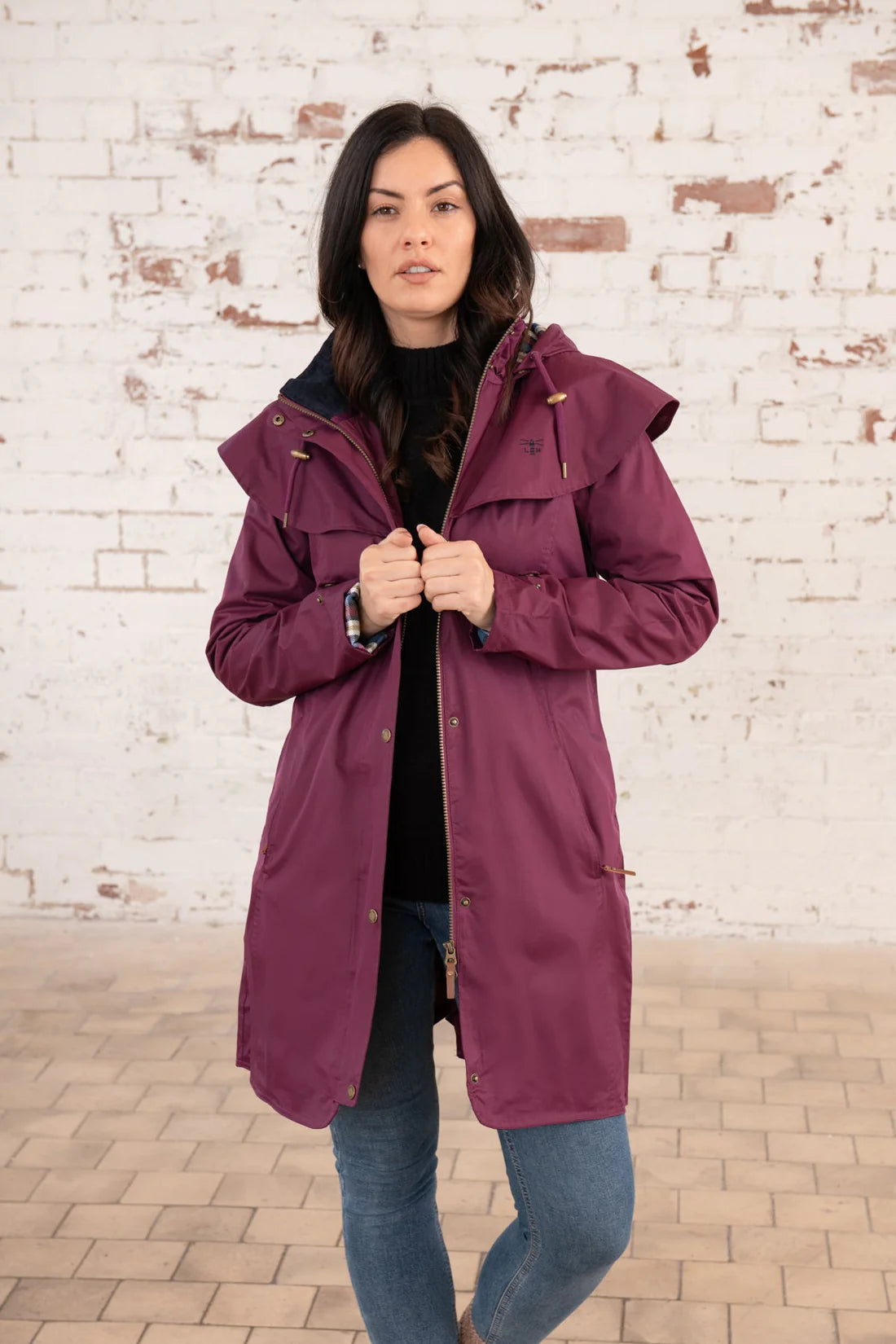 Woman wearing a purple raincoat against a white brick wall.