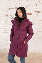 Woman wearing a purple raincoat against a white brick wall.