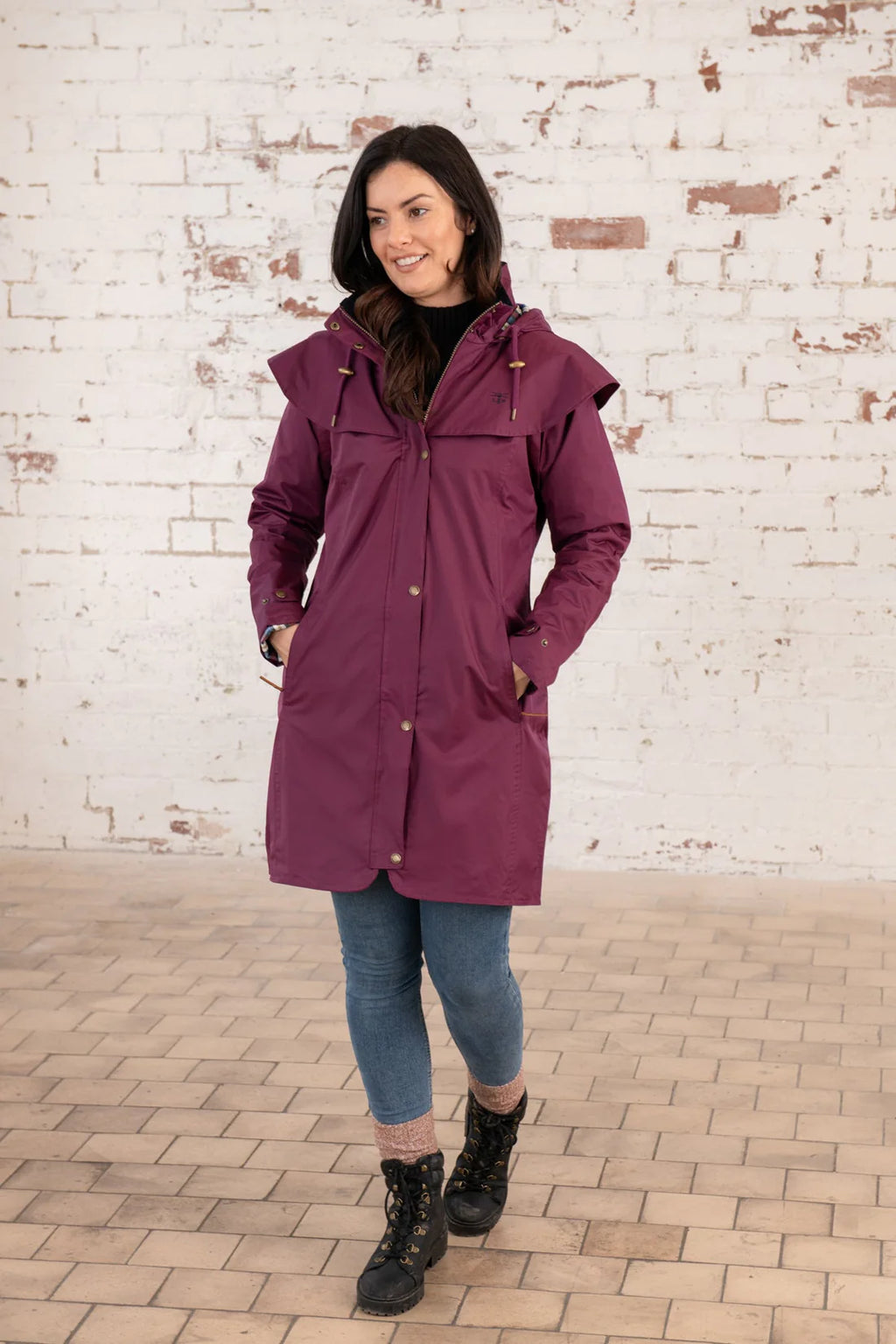 Woman wearing a purple raincoat standing against a brick wall.