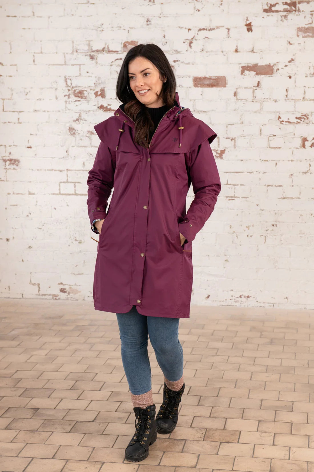 Woman wearing a purple raincoat standing against a brick wall.