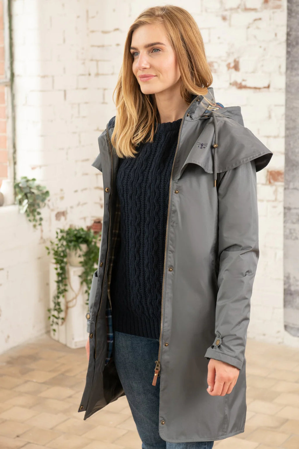 Woman wearing a gray raincoat standing in front of a brick wall.