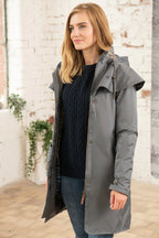 Woman wearing a gray raincoat standing in front of a brick wall.