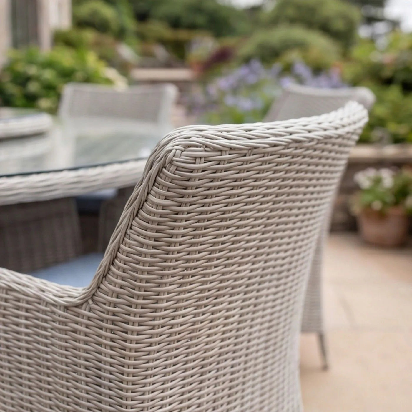 A close-up of a light gray woven outdoor patio chair in a garden patio setting.
