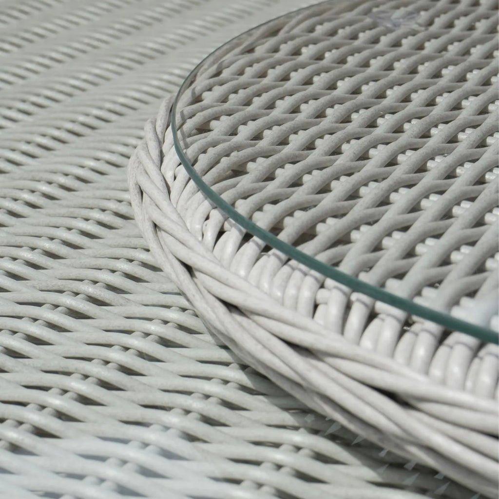 Close-up of a round table with a white woven wicker or rattan-style mesh surface and a clear glass tabletop edge.