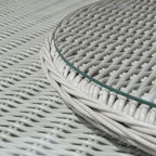 Close-up of a round table with a white woven wicker or rattan-style mesh surface and a clear glass tabletop edge.