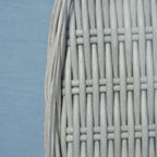 Close-up of a light gray woven wicker or rattan material with vertical strands interlaced horizontally, shown against a pale blue background.