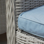 A close-up of a light blue outdoor cushion resting on a white-washed wicker chair.