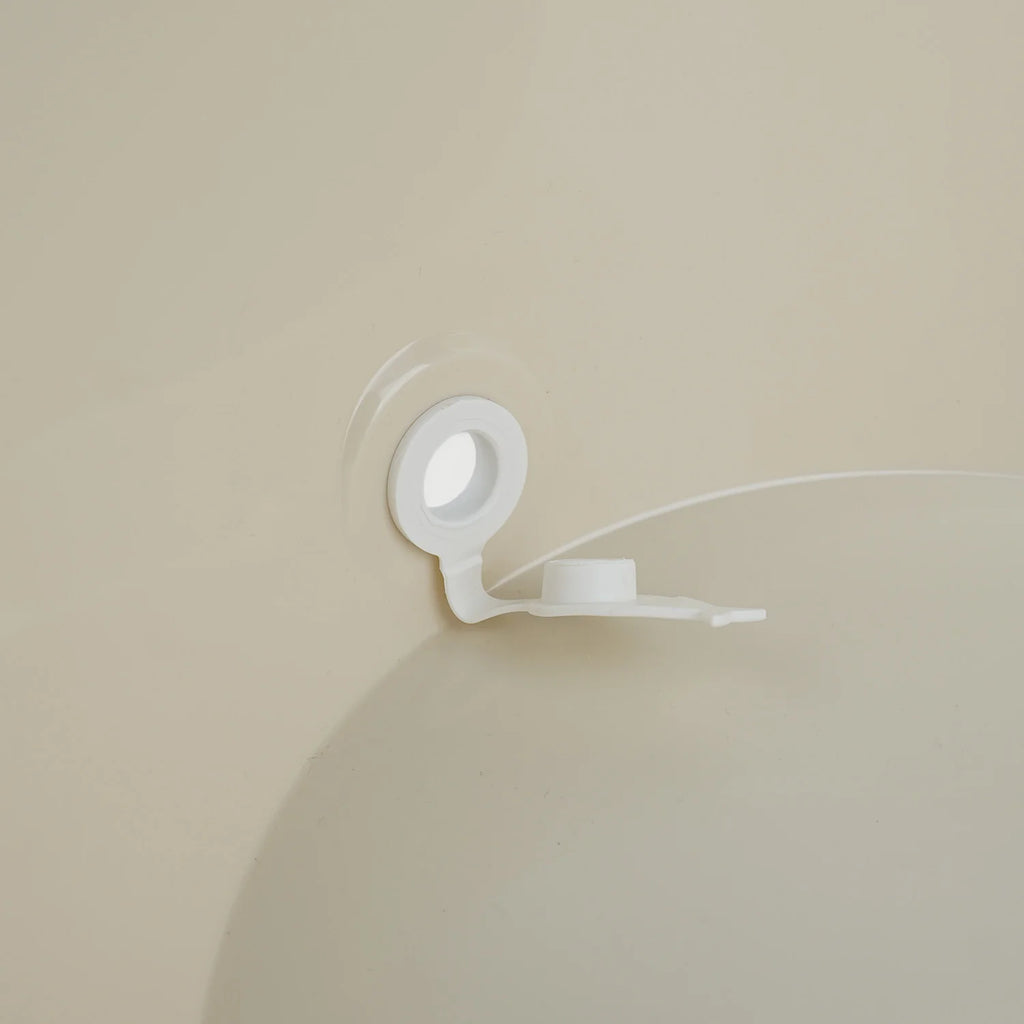 A white plastic cap remover tool with a circular suction base and a small hook-like arm, shown attached to a beige bath tub surface with a clear suction ring.