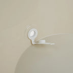 A white plastic cap remover tool with a circular suction base and a small hook-like arm, shown attached to a beige bath tub surface with a clear suction ring.