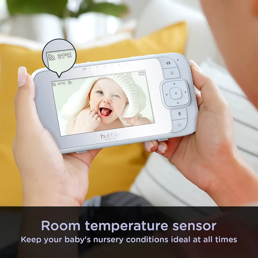 Person holding a baby monitor with a screen displaying a baby's face, with text about room temperature sensor.
