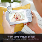 Person holding a baby monitor with a screen displaying a baby's face, with text about room temperature sensor.