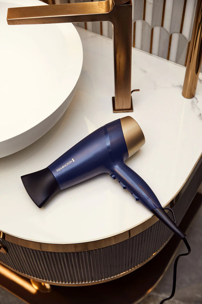 Blue hair dryer on a round marble table with a gold faucet in the background