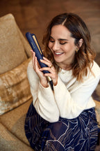 Woman holding a blue hair straightener in a cozy indoor setting