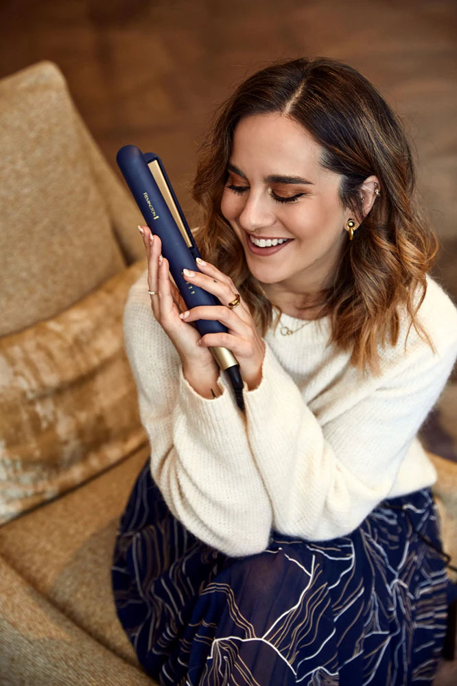 Woman holding a blue hair straightener in a cozy indoor setting