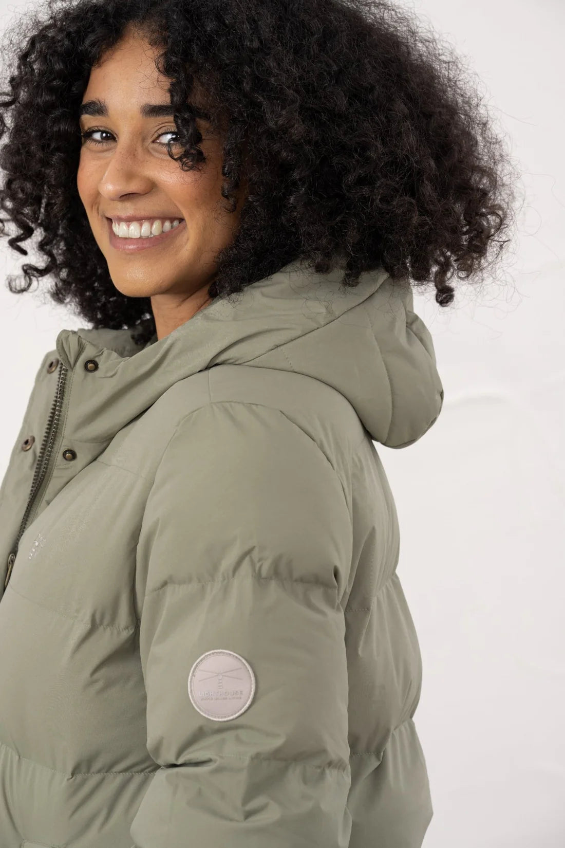 Woman wearing a green puffer jacket with a visible brand logo on a white background