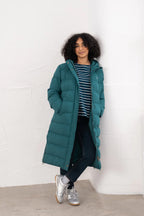 Person wearing a teal puffer coat against a white brick wall.
