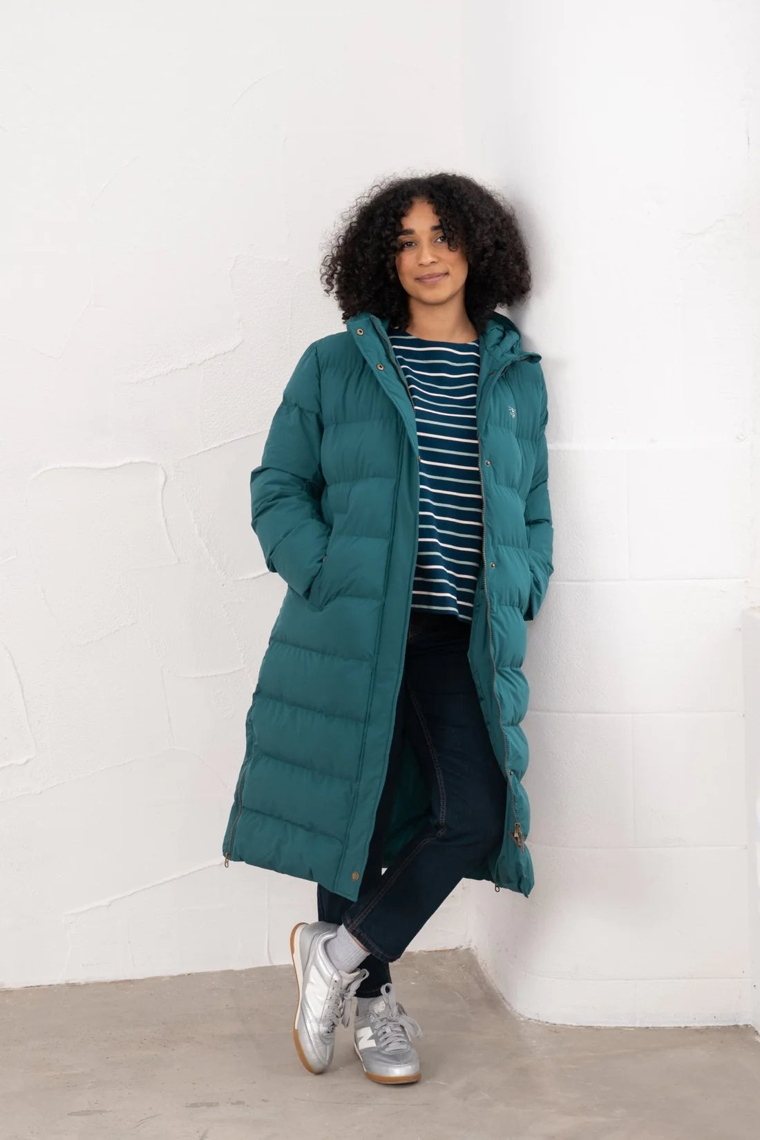 Person wearing a teal puffer coat against a white brick wall.
