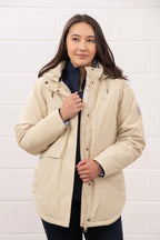 Woman wearing a beige jacket against a white tiled wall