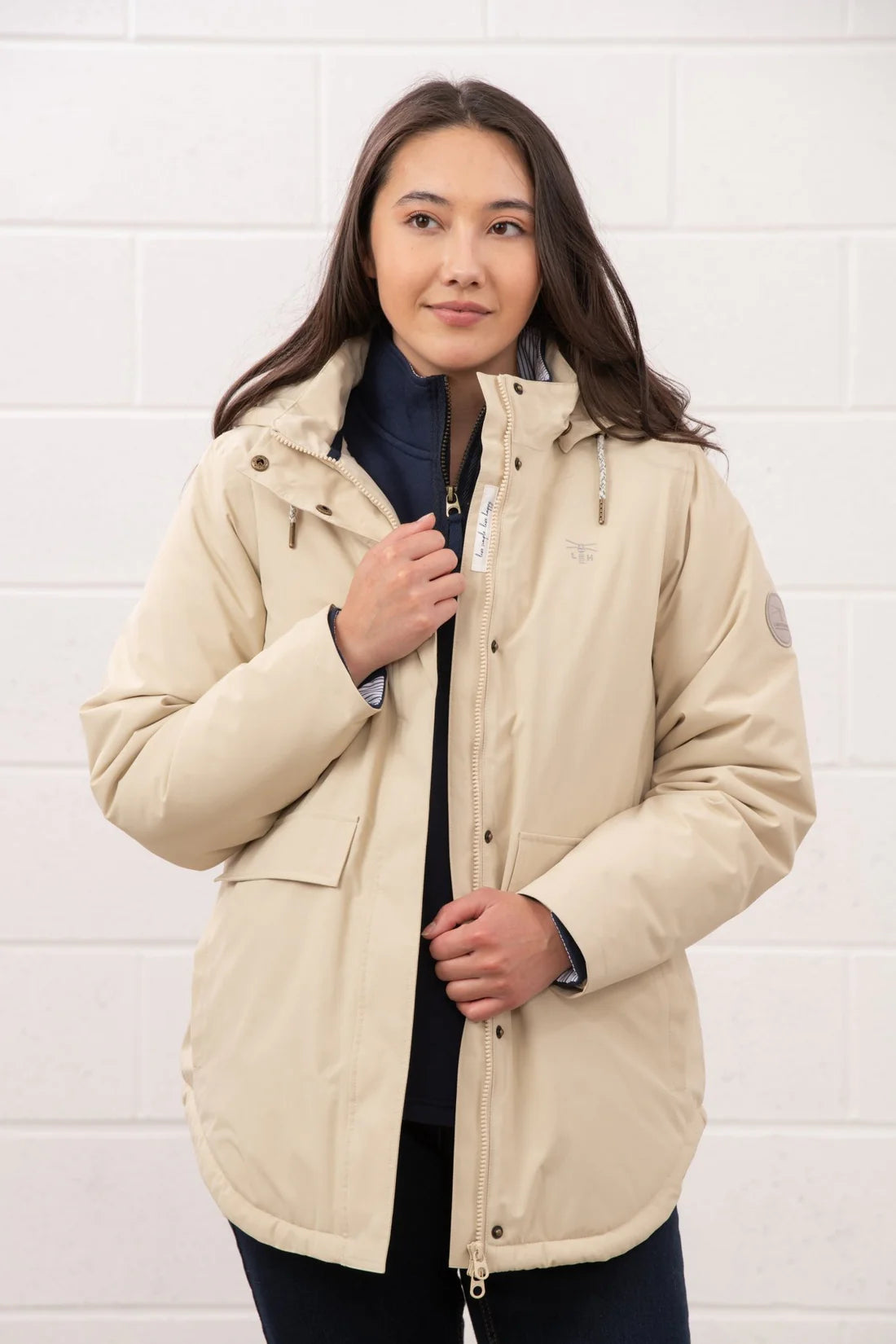 Woman wearing a beige jacket against a white tiled wall