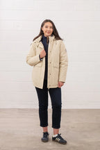 Person wearing a beige coat standing against a white wall.