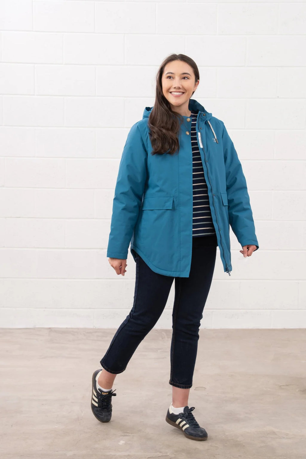 Woman wearing a blue jacket standing against a white wall.