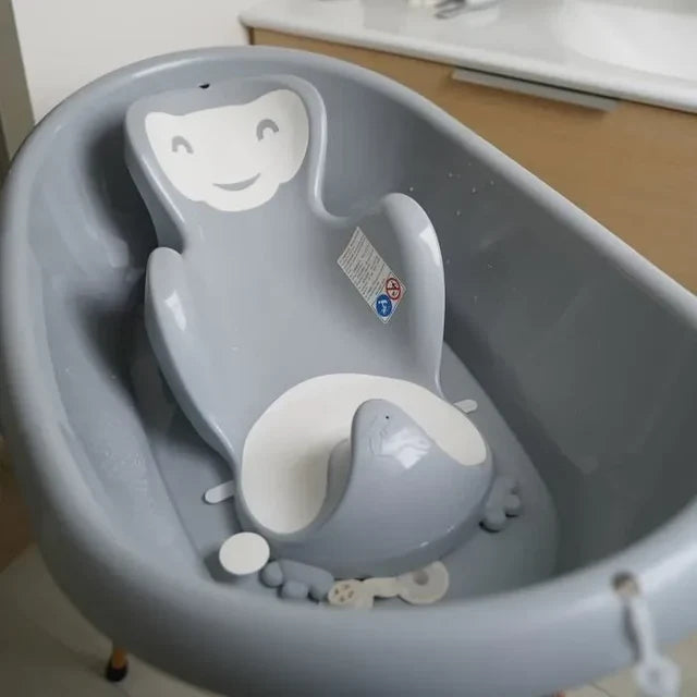 Gray baby bathtub with a smiley face design on a wooden floor.