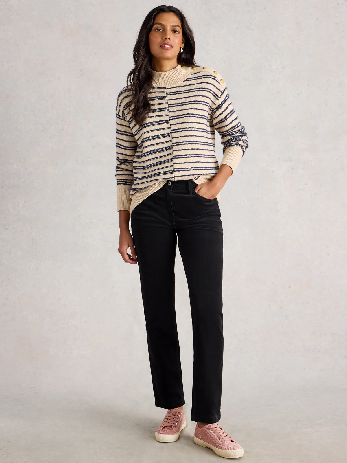 Woman wearing a striped sweater and black pants against a plain background