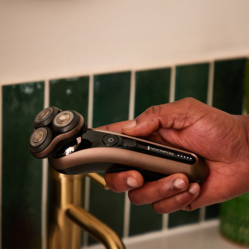 Hand holding a electric shaver with a tiled bathroom background
